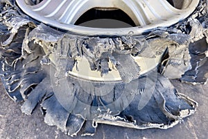 A discarded burst tire with crushed and damaged rubber. A passenger car tire on an alloy rim, torn into pieces. The tire