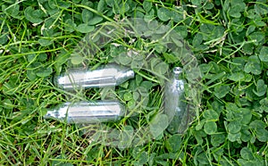 Discarded laughing gas canisters in the grass: metal vials containing nitrous oxide gas, used for whipping cream, but also as a le