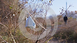 A Discarded Medical Mask Sways on the Wind on a Dry Tree Branch in Forest. 4K