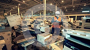 Discarded office machines with a male expert inspecting them. Electronic garbage recycling factory.
