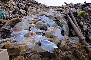 Discarded used medical face masks along and garbage trash with other plastic debris lies