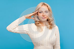 Disciplined and responsible blond woman in knitted sweater holding hand near head saluting, patriotic gesture, honor and dignity