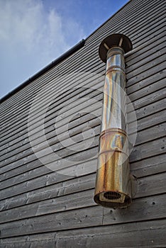 Discoloured stainless steel exhaust chimney, on wooden panelled building. Charmouth, Dorset.