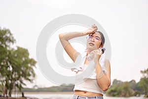 A discomfort woman holds a water bottle while wiping her forehead, standing outdoors on a hot day