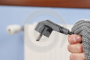 Disconnected electric plug of a convector heater in a frozen hand in a warm sweater