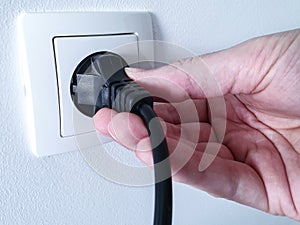Disconnecting black electrical power plug with a hand inside a white plastic power socket