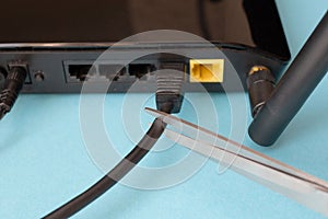 Disconnecting the Internet. Black router on a blue background. Man wants to cut the wire for the Internet with scissors.