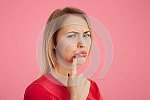 Discontent young beautiful female with unhappy look, has oral herpes, indicates at wound near lips, stands sideways against pink b photo