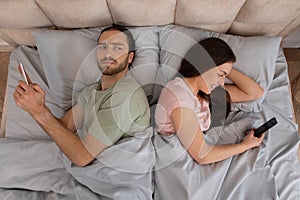 Discontent young couple using phones in bed, disconnected