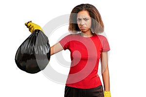 Discontented, frowning girl pouts, feels stench, picks up black garbage bag in yellow rubber gloves, looks disgusted