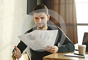 Discontented Office Worker Looking At Documents Sitting In Modern Office