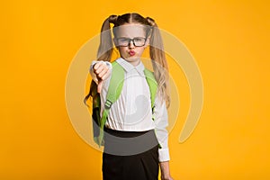 Discontented Schoolgirl Gesturing Thumbs Down Over Yellow Background