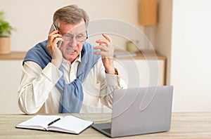Discontented Senior Man Talking On Phone Sitting In Modern Office