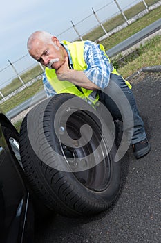 Discouraged retired man unable to change car tyre photo