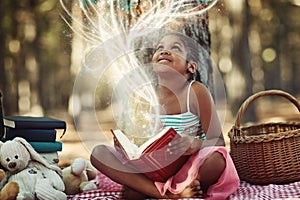 Discovering the magic of reading. a little girl reading a book with glowing pages in the woods.