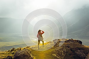 Discovery Travel Destination Concept. Hiker Young Woman With Backpack Rises To The Mountain Top Against Backdrop Of Sunset, Rear V