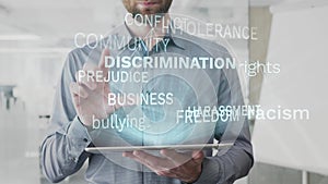 Discrimination, racism, prejudice, rights, bullying word cloud made as hologram used on tablet by bearded man, also used