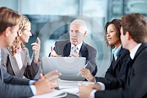 Discussing their next hostile takeover. Business executives sitting at a table during a meeting and using a laptop.