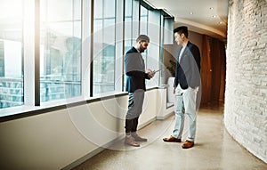 Discussing what needs to be discussed. two young businessmen using a digital tablet together in a modern office.