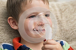 Diseased child with inhaler. Sick boy with clear oxygen mask. Cute boy inhalation therapy by the mask of inhaler