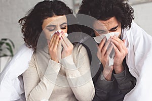 diseased young couple blowing noses into napkins