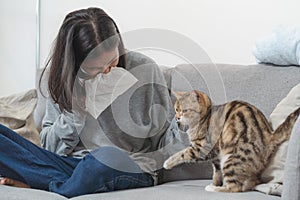 Diseases from pets concept. Woman sneezing from fur allergy on the sofa and playing with her cat