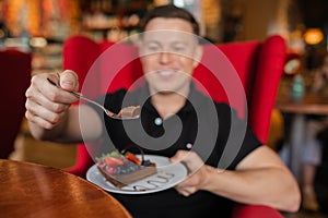 Disfocused man holds out slice of chocolate dessert on spoon to the camera