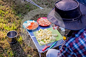 Camp cooking process. A man preparing vegetables to make a stew on a campfire. Camping life