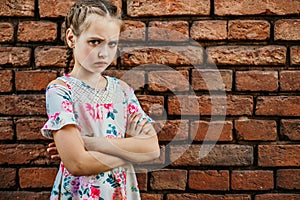 Disgruntled girl frowns, stands upset against a brick wall