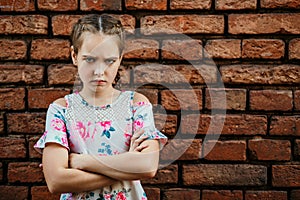 Disgruntled girl frowns, stands upset against a brick wall