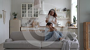 Disgruntled mother is talking on phone and arguing with husband walking near daughter sits on couch