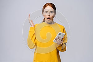 Disgruntled young woman holding mobile phone and looking at camera on isolated white background.