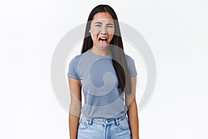 Disgusted asian young girl cringe from awful smell, sticking out tongue, squinting and wrinkle nose from aversion, toop photo