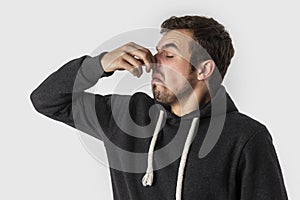 Disgusted caucasian young man holding his nose to avoid bad smell. Isolated on white background