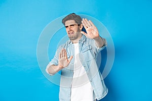 Disgusted guy saying no, refusing and looking away from something awful, cringe while standing against blue background