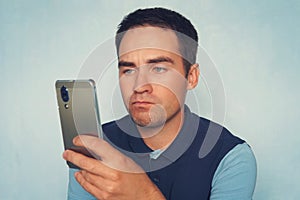 A sad expression on the face of a young man holding a modern smartphone on a blue background