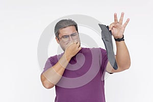 A disgusted middle aged man covers his nose while holding a smelly sock in his hand. Isolated on a white background