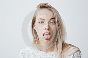 Disgusted pretty young woman with blonde hair sticking out tongue, expressing her dislike or disregard towards something photo
