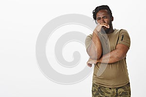 Disgusted unhappy dark-skinned man in military outfit, covering nose with palm from reek or awful smell, expressing photo