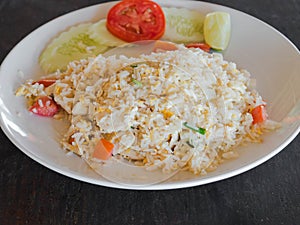 Dish of Asian cuisine - fried white rice with egg, chicken meat and vegetables on a white plate on the wood table in a Thai