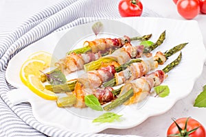 A dish of asparagus and bacon on a white plate. Baked green asparagus wrapped in bacon. Healthy food