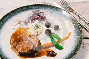 A dish of beef fillet with sauce and vegetables on white marble table.