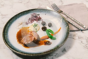 A dish of beef fillet with sauce and vegetables on white marble table.