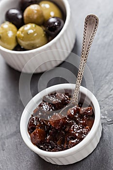 A dish of chutney and a dish of black and green olives photo