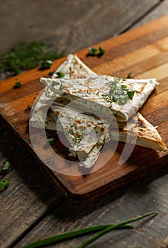 A dish of cottage cheese with parsley and onions in pita bread fried on a grate lie on a board