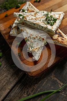 A dish of cottage cheese with parsley and onions in pita bread fried on a grate lie on a board