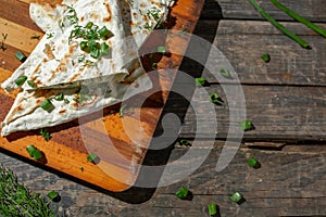 A dish of cottage cheese with parsley and onions in pita bread fried on a grate lie on a board