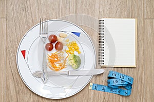 Dish with cutlery, healthy food, tape measure and a notebook on a wooden background