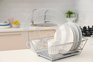 Dish drainer with clean dinnerware on table in kitchen