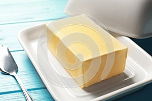 Dish with fresh butter and knife on wooden background